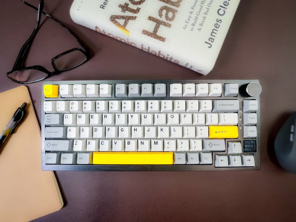 Desk scene with a mechanical keyboard, glasses, notebook, and book on a brown leather mat